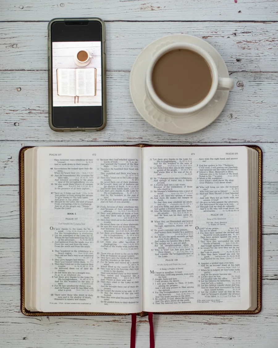 An open Bible beside a cup of coffee and a phone
