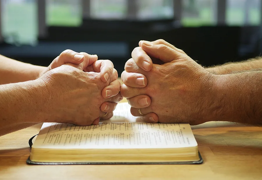 Two people praying over an open Bible